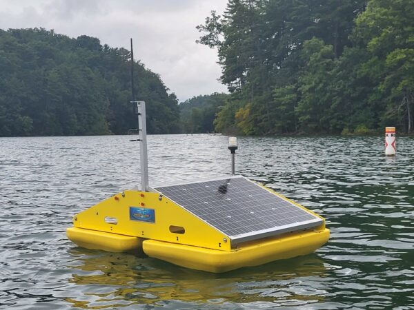 A floating yellow ultrasonic algae control raft with attached solar panels to power the ultrasonic transducer unit that is suspended into the water below the raft